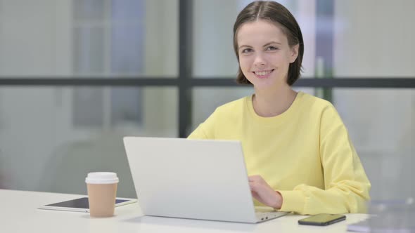 Young Woman Smiling at Camera While Using Laptop in Office