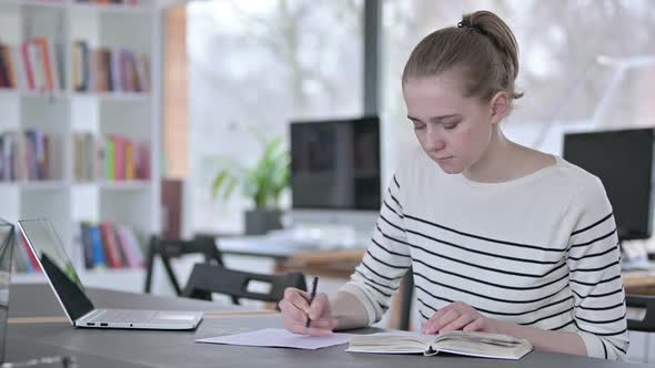 Young Woman Reading Book and Doing Paperwork in Library