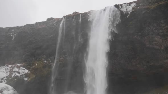 Static, slow motion, tilt shot, of water streaming down on snowy ground, at Seljalandfoss waterfall,