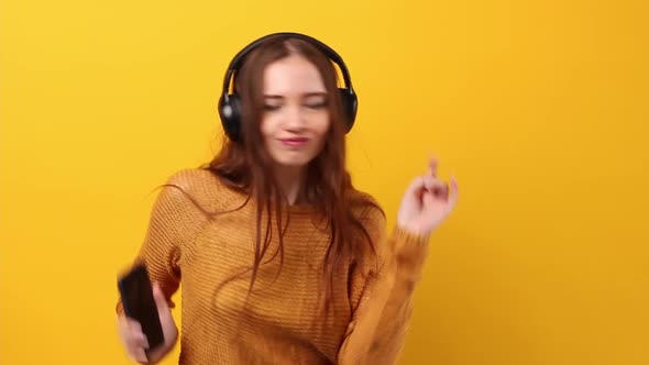 Woman Listening to Music in Black Headphones in the Studio on Pastel Yellow Background and Dancing