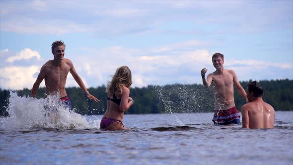 Young adults splashing a girl while playing in a lake.