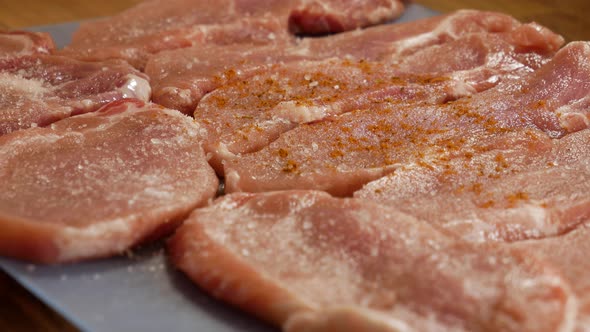 Pouring red spices on raw pork meat steaks in close up view