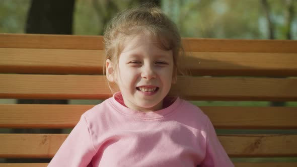 Smiling Little Girl Shows Thumbsup on Bench in Spring Park
