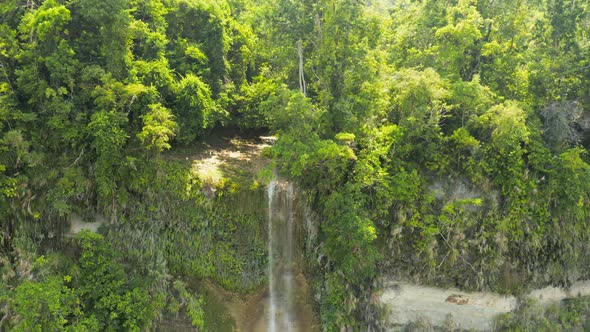 Aerial drone view descending down a tall waterfall in the jungle