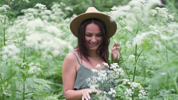 Young Beautiful Woman Posing in a Forest with a Hat on a Background of White Flowers. Happy Brunette