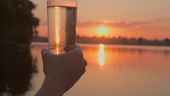 Human Hand Holds Misted Glass of Water at Sunset By the River