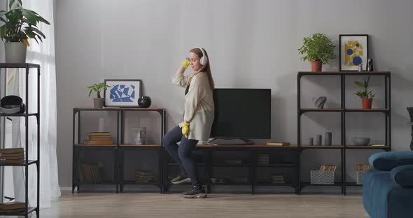 Funny Housewife Is Dancing During Cleanup and Dusting in Apartment Listening To Music By Headphones