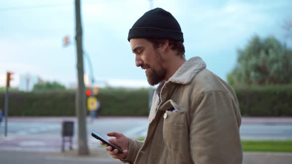 Handsome man wearing hat walking and typing on mobile