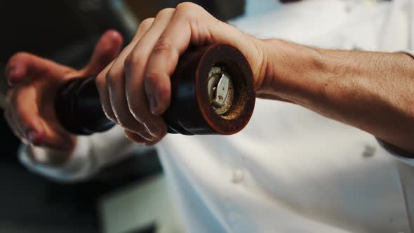 Close up: the chef is using pepper mill to add some pepper to his food, pepper is falling