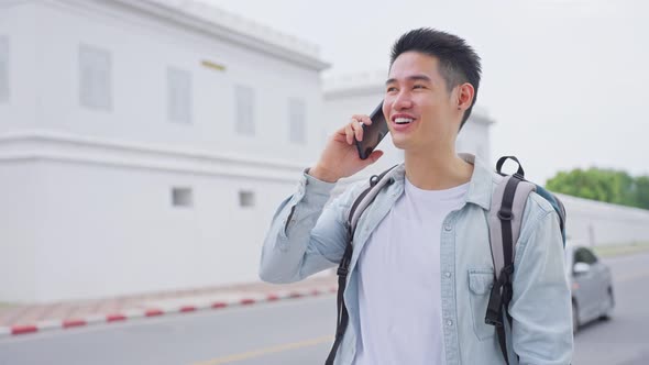 Asian attractive young man backpacker talking on phone walk in city enjoy spend time on holiday trip