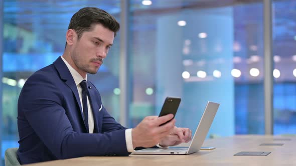 Businessman Using Smartphone and Laptop at Work