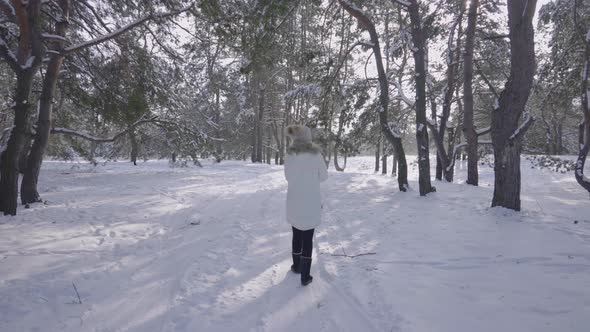 Back View of Girl in Winter Down Coat Walks Along Path in Snowy Winter Forest