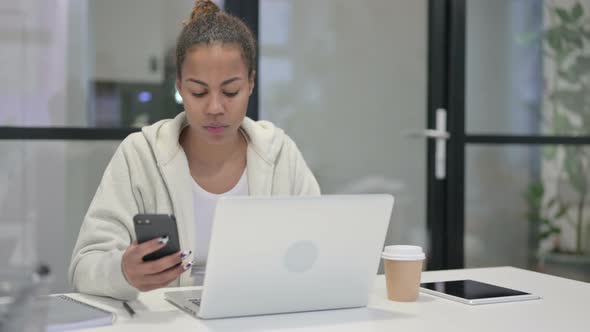 African Woman Using Smartphone While Using Laptop in Office