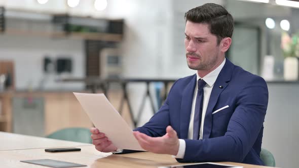 Disappointed Businessman Reading Documents in Office 
