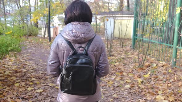 A Brunette with Short Hair in a Brown Jacket Walks in the Park on a Sunny Autumn Day