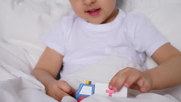 Child Playing in the Car Wooden Ambulance Toy on the Bed at Home