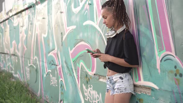 Young Modern Woman Uses a Smartphone Against a Wall with Street Graffiti