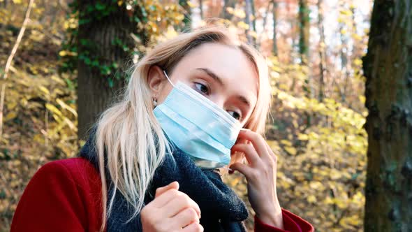 Portrait of a young beautiful woman putting on Corona safety mask amidst orange brown autumn forest