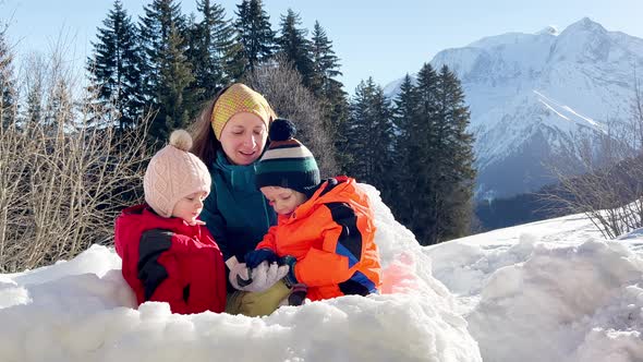 Mother with Girl and Boy Play Together in the Snow Fortress