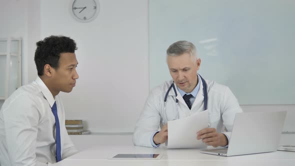 Senior Doctor Talking with Patient in Clinic, Discussing Medical Report