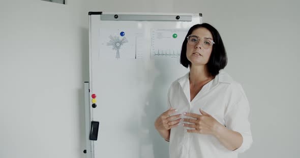 Female Speaker Explaining Topic with Gesturing in Front of Camera at Whiteboard