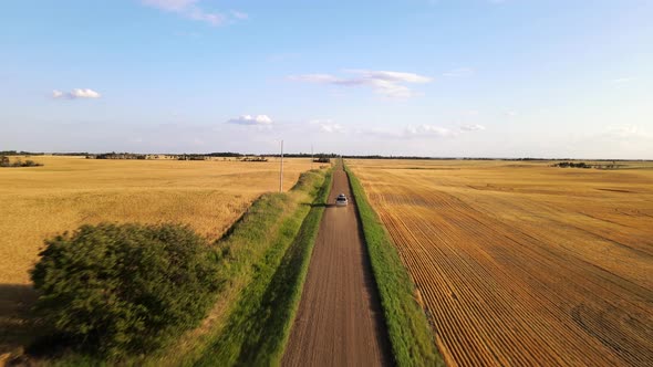 4k drone shot following silver car driving along dusty dirt road during sunset. Straight road line b