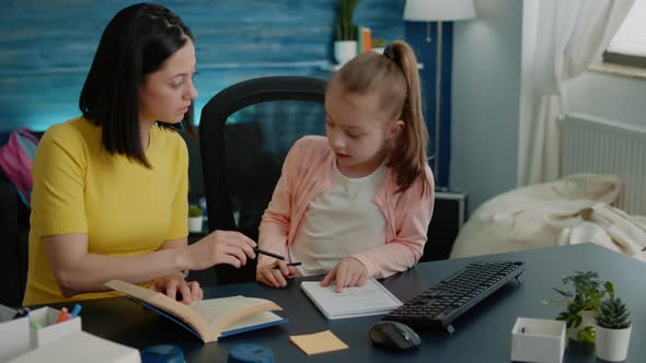 Parent Using Books to Help Little Girl with Homework at Desk