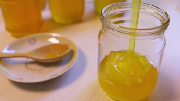 Woman Pours Honey Into Transparent Jars on a White Table