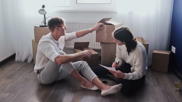 Happy Couple Open Prepare Cardboard Boxes to Moving Out Family Sitting on Floor in Living Room on