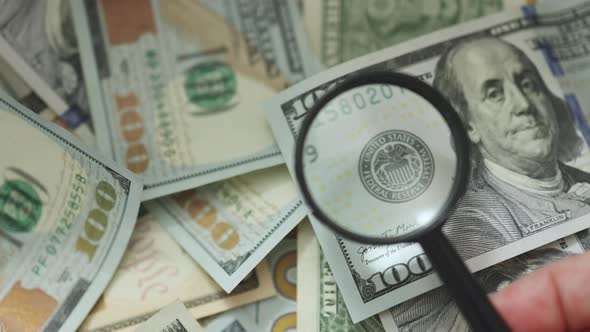 Magnifying Glass on Hundred Dollar Bill Checking Examine Inspecting Money