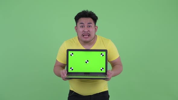 Happy Young Overweight Asian Man Showing Laptop and Looking Surprised