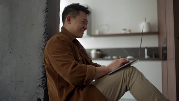 Positive Asian man wearing casual cloth typing on laptop