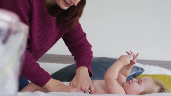 Caucasian mother changing diaper of her baby on the bed at home