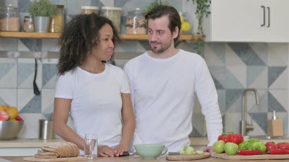 Serious Mixed Race Couple Talking While Standing in Kitchen