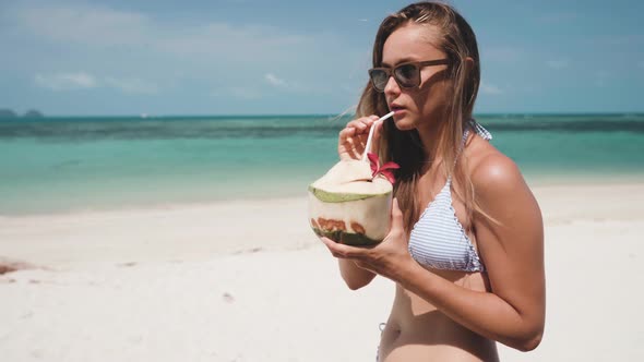 Woman Drinking Fresh Coconut Water with Straw on Beach
