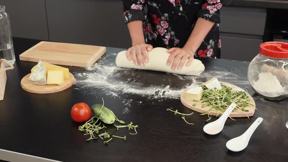 Woman rolling dough by hands. Female in professional kitchen prepares dough with flour for pizza