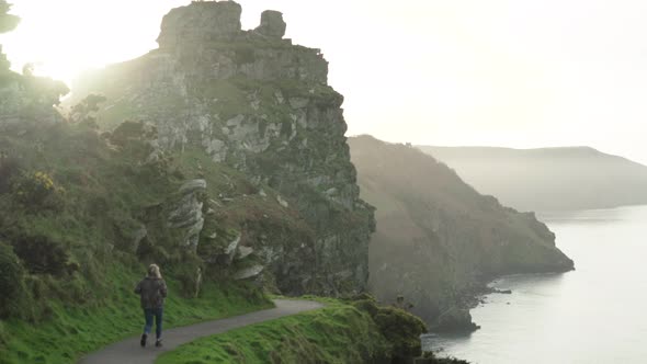 Lone Woman Walking Along The Road On The Valley Of Rocks By The Coast In North Devon, England During