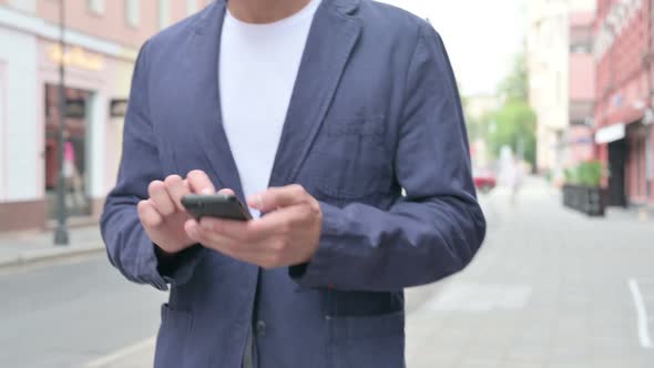 Close Up Shot of Hands of Man Browsing Internet on Smartphone While Walking Down the Street