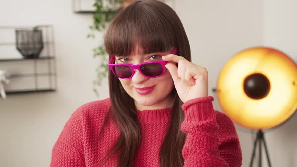 Sassy Caucasian Young Adult Woman Looking at Camera and Touching Her Pink Sunglasses While Standing