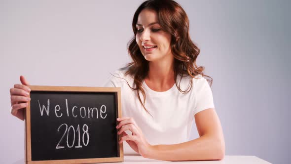 Portrait of smiling woman showing slate with text welcome 2018 4k