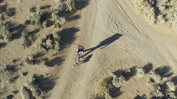 Aerial shot of a young man backpacking with his dog on a dirt road in a mountainous desert