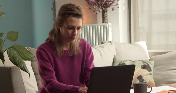 Woman on the sofa talking in front of a laptop in a business meeting video call while she is watchin