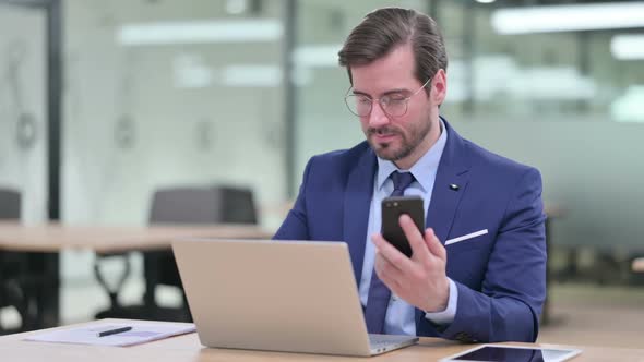 Professional Young Businessman Using Smartphone and Laptop