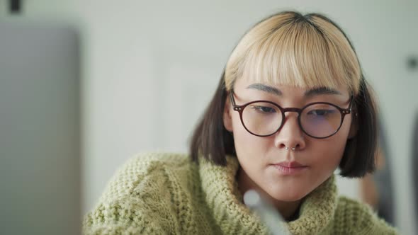 Handsome Asian woman in eyeglasses writing something in notepad from laptop