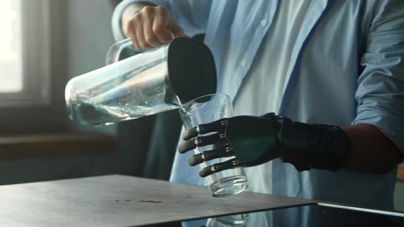 Disabled guy with bio hand prothesis pours water into glass from bowl