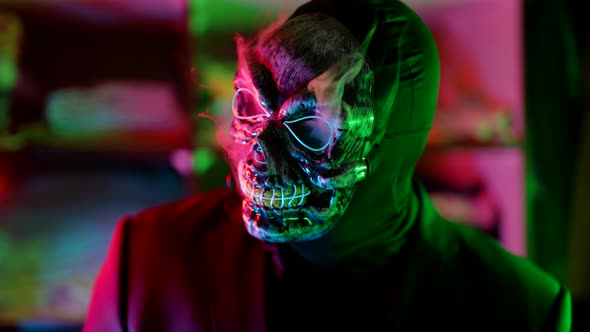 a Man in a Scary Glowing Death Mask Looks to the Side and Lets Out Puffs of Smoke in a Neon Flashing