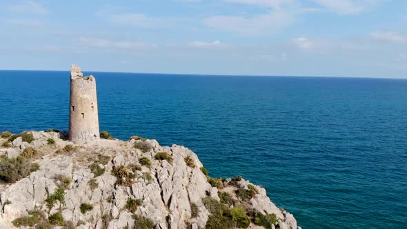 Drone flies over a coastal watchtower, centennial tower on the blue sea cliff and rocks in a beautif