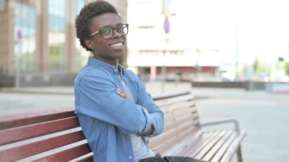 Young African Man Smiling at Camera While Sitting on Bench
