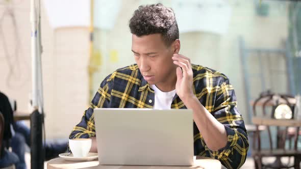 Young African Man with Neck Pain Using Laptop, Outdoor Cafe