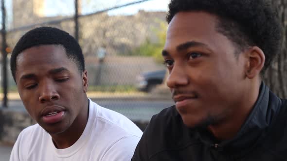 Two young basketball players talking on the sidelines of a street court.